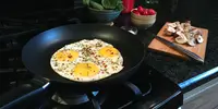 Three eggs frying in a nonstick skillet on a gas cooktop.