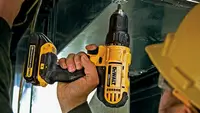 Photo of a person in a yellow helmet and safety glasses using a DeWalt drill.