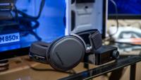 A gaming headset in black rests on a desk with gaming monitor behind it.
