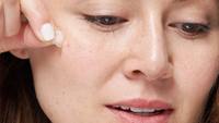 A woman taking a pimple patch off of her face.