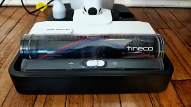 A Tineco vacuum head sits on its base on a wooden floor