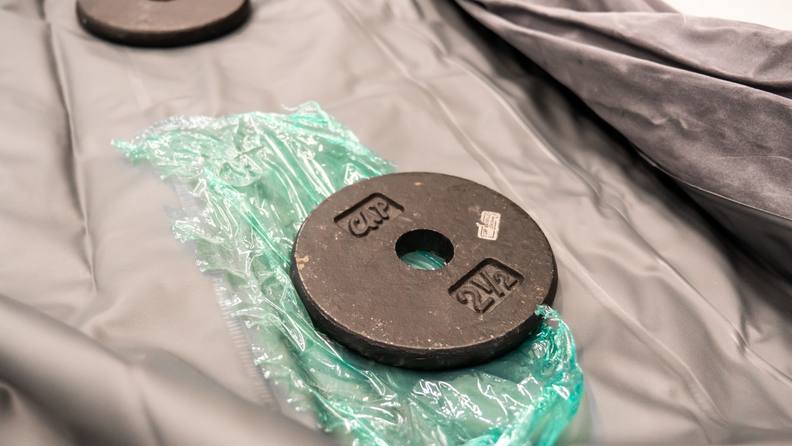 An iron weight next to the patched hole on the air mattress.