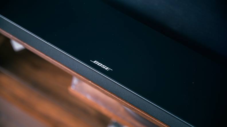 The all-black Bose TV Speaker positioned on an entertainment center made of rich brown wood.