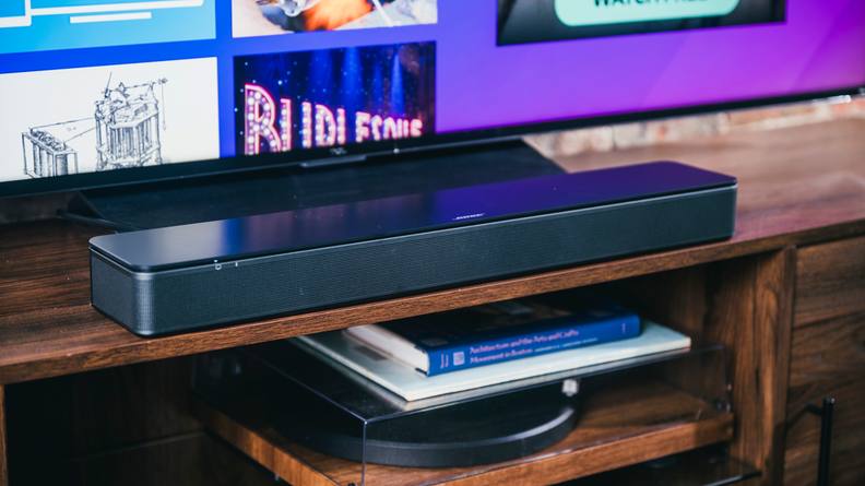 The all black Bose TV Speaker soundbar positioned under a TV on a wooden entertainment cabinet, set above a record player.
