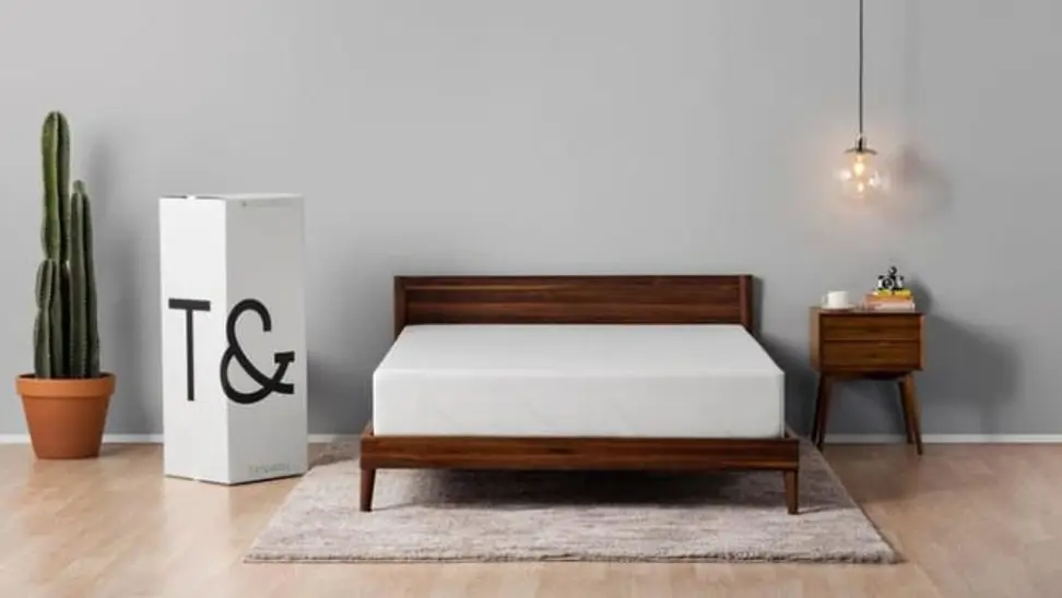 A bare Tuft and Needle mattress, sitting on a wooden bed frame in a master bedroom.