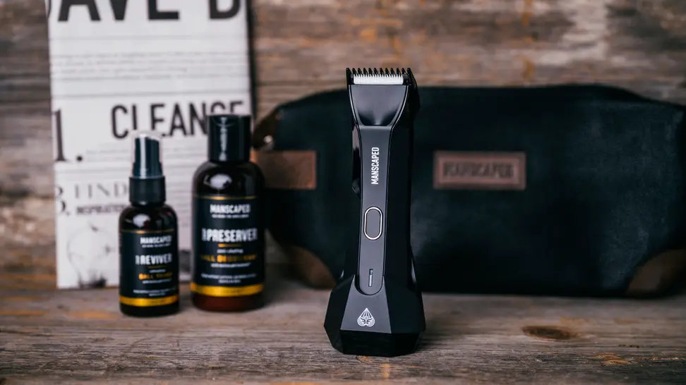 The contents of the Manscaped Perfect Package, which includes the trimmer, two bottles of product, a fake newspaper, and a toiletry bag.