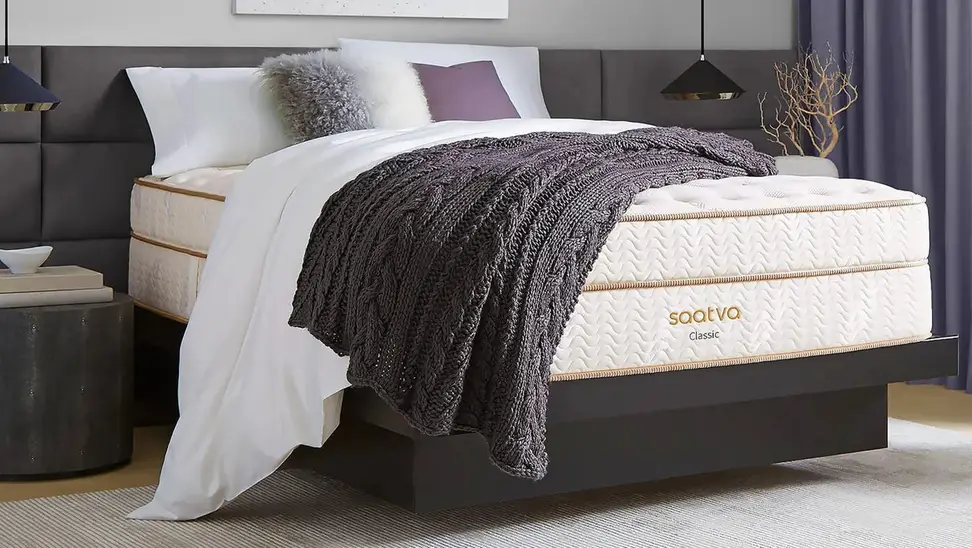 Image of a bedroom with a Saatva mattress covered with pillows and a throw blanket.