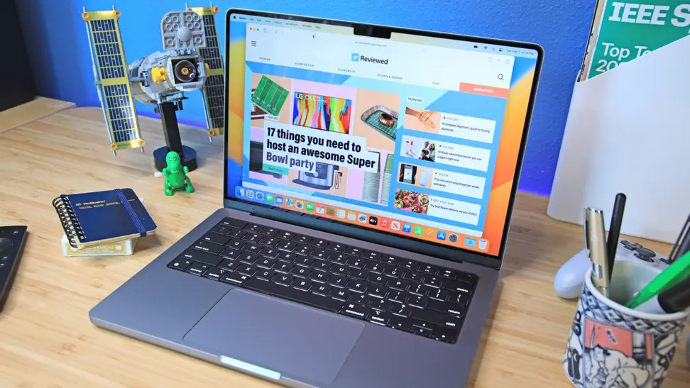 A new Apple laptop flipped open and turned on, sitting on top of a desk with several objects